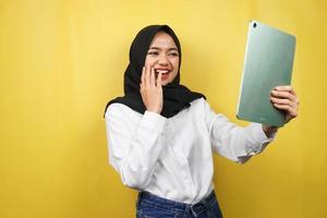 Schöne junge asiatische muslimische Frau lächelnd, aufgeregt und fröhlich mit Tablet, isoliert auf gelbem Hintergrund foto
