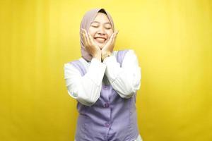 schöne junge asiatische muslimische Frau, die glücklich lächelt, süß, sich wohl fühlt, sich umsorgt fühlt, sich gut fühlt, mit Händen, die Wangen einzeln auf gelbem Hintergrund halten foto