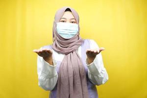 muslimische Frau mit medizinischer Maske, Hände, die etwas präsentieren, isoliert auf gelbem Hintergrund