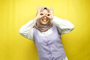 schöne asiatische junge muslimische frau, die fröhlich und aufgeregt lächelt, mit brillenhänden, isoliert auf gelbem hintergrund foto