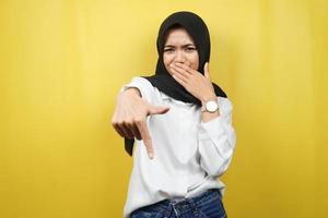 Schöne junge muslimische Frau mit der Hand, die den Mund bedeckt, die Hand nach unten zeigt, einen missbilligenden Ausdruck zeigt, Ekel über etwas zeigt, isoliert auf gelbem Hintergrund foto