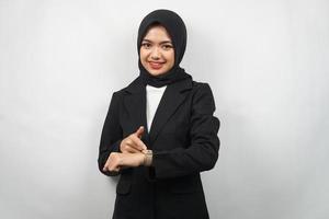 schöne junge asiatische muslimische Geschäftsfrau selbstbewusst und lächelnd, mit den Händen auf die Uhr, Zeit für die Arbeit, die Zeit ist abgelaufen, Arbeitsfrist, einzeln auf grauem Hintergrund foto