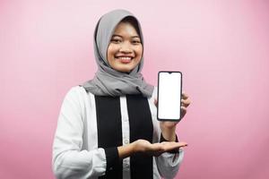 Schöne junge asiatische muslimische Frau, die selbstbewusst und aufgeregt mit den Händen lächelt, die Smartphone halten, App präsentieren, etwas präsentieren, isoliert auf rosa Hintergrund, Werbekonzept