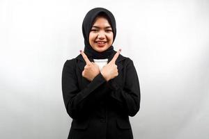 Schöne junge asiatische muslimische Geschäftsfrau, die selbstbewusst, enthusiastisch, fröhlich lächelt, mit den Händen, die auf leeren Raum zeigen, etwas präsentieren und die Kamera einzeln auf weißem Hintergrund betrachten foto