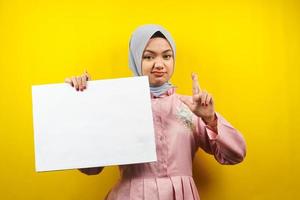 hübsche junge muslimische Frau, die fröhliche leere leere Banner, Plakate, weiße Tafeln, leere Schilder, weiße Werbetafeln hält, etwas im Kopierraum präsentiert, Werbung foto