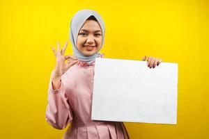 hübsche junge muslimische Frau, die fröhliche leere leere Banner, Plakate, weiße Tafeln, leere Schilder, weiße Werbetafeln hält, etwas im Kopierraum präsentiert, Werbung foto