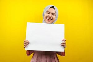 hübsche junge muslimische Frau, die fröhliche leere leere Banner, Plakate, weiße Tafeln, leere Schilder, weiße Werbetafeln hält, etwas im Kopierraum präsentiert, Werbung foto