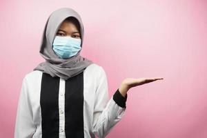 muslimische frau mit medizinischer maske, hände, die etwas im leeren raum präsentieren, isoliert auf rosa hintergrund