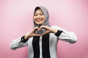 Schöne asiatische junge muslimische Frau, die selbstbewusst, enthusiastisch und fröhlich lächelt, mit Handzeichen der Liebe, Zuneigung, glücklich, auf der Brust einzeln auf rosafarbenem Hintergrund