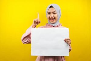 hübsche junge muslimische Frau, die fröhliche leere leere Banner, Plakate, weiße Tafeln, leere Schilder, weiße Werbetafeln hält, etwas im Kopierraum präsentiert, Werbung foto