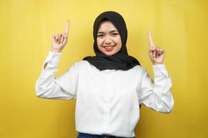 schöne junge asiatische muslimische frau, die selbstbewusst, enthusiastisch und fröhlich lächelt, mit den händen, die nach oben zeigen, etwas präsentieren, die kamera einzeln auf gelbem hintergrund betrachtend, werbekonzept foto