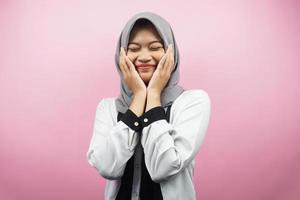 schöne junge asiatische muslimische Frau, die glücklich lächelt, süß, sich wohl fühlt, sich umsorgt fühlt, sich gut fühlt, mit Händen, die Wangen einzeln auf rosafarbenem Hintergrund halten