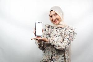 Schöne junge asiatische muslimische Frau, die selbstbewusst und aufgeregt mit den Händen lächelt, die Smartphone halten, App bewerben, etwas fördern, isoliert auf weißem Hintergrund, Werbekonzept foto
