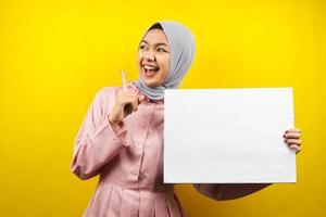 hübsche junge muslimische Frau, die fröhliche leere leere Banner, Plakate, weiße Tafeln, leere Schilder, weiße Werbetafeln hält, etwas im Kopierraum präsentiert, Werbung foto