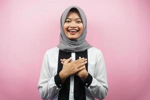 schöne junge asiatische muslimische frau, die überrascht und fröhlich lächelt, mit den händen, die die brust halten, aufgeregt, nicht erwartet, die kamera einzeln auf rosa hintergrund betrachtend foto