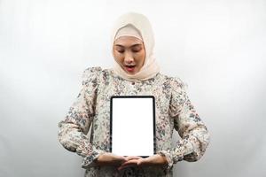 schöne junge asiatische muslimische frau lächelnd, aufgeregt und fröhlich, die tablette mit weißem oder leerem bildschirm hält, app fördert, produkt fördert, etwas präsentiert, isoliert auf weißem hintergrund