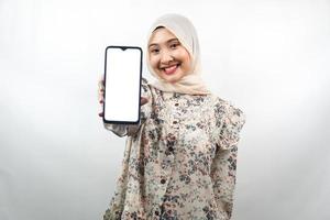 schöne junge asiatische muslimische frau, die selbstbewusst, enthusiastisch und fröhlich lächelt, mit den händen, die das smartphone halten, die anwendung fördern, etwas fördern, isoliert auf weißem hintergrund