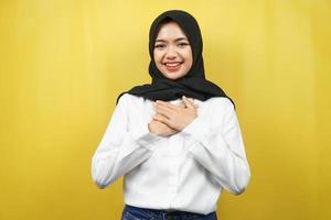 schöne junge asiatische muslimische frau, die überrascht und fröhlich lächelt, mit den händen, die die brust halten, aufgeregt, nicht erwartet, die kamera einzeln auf gelbem hintergrund betrachtend