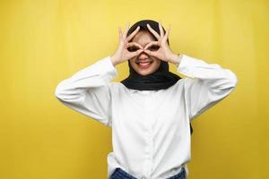 schöne asiatische junge muslimische frau, die fröhlich und aufgeregt lächelt, mit brillenhänden, isoliert auf gelbem hintergrund foto