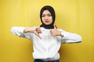 schöne asiatische junge muslimische frau mit handzeichen wie oder abneigung, ja oder nein, glücklich oder traurig, vergleicht zwei dinge, einzeln auf gelbem hintergrund
