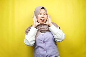 schöne junge asiatische muslimische frau schockiert, überrascht, wow-ausdruck, mit händen, die wange halten, isoliert auf gelbem hintergrund foto