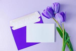 Umschlag mit Einladung zum Urlaub und Strauß Tulpen auf lila Hintergrund. Trendfarbe des Jahres 2022. foto