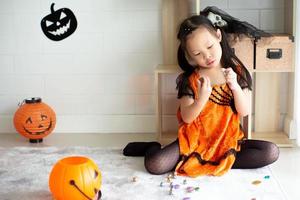 Portrait asiatisches kleines Mädchen wirft und isst Süßigkeiten und Schokolade aus Süßes oder Saures mit Halloween-Thema im Hintergrund foto