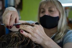 Frau mit Gesichtsmaske, die sich die Haare mit Schere und Kamm schneidet foto