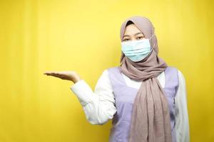 muslimische frau mit medizinischer maske, hände, die etwas im leeren raum präsentieren, isoliert auf gelbem hintergrund foto