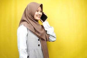 Schöne junge asiatische muslimische Frau, die selbstbewusst und fröhlich lächelt und jemanden anruft, mit Blick auf leeren Raum, isoliert auf gelbem Hintergrund, Werbekonzept foto
