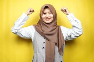 schöne asiatische junge muslimische frau mit angehobenen muskeln, kraftzeichenarme, isoliert auf gelbem hintergrund