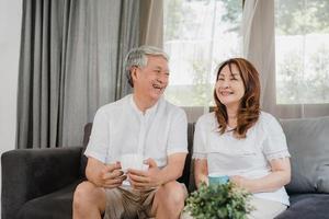 asiatisches älteres paar entspannen sich zu hause. Asiatische ältere chinesische Großeltern, Ehemann und Ehefrau lächeln, reden und trinken Kaffee, während sie auf dem Sofa im Wohnzimmer zu Hause liegen.