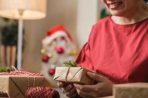 Frau, die handgemachte Weihnachtsgeschenkbox mit braunem Papier, das mit Weihnachtsdekor auf Holztisch verzieht, herstellt