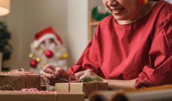 Frau, die Geschenkanhänger schreibt und an Weihnachtsgeschenk auf Holztisch anbringt