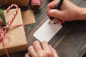 Frau, die Geschenkanhänger schreibt und an Weihnachtsgeschenk auf Holztisch anbringt