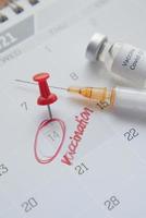 Impftag Konzept Glasampulle mit Impfstoff und Spritze auf Kalender foto