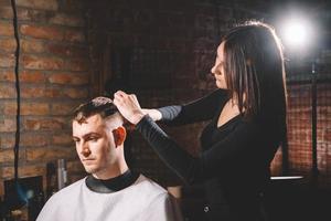 Schöne Friseurin, die in einem Friseurladen die Haare des Kunden mit einer Schere schneidet foto