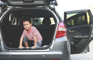 ein Junge, der ungezogen auf dem Kofferraum eines Autos spielt foto