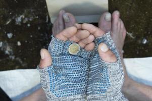 eine Münze in den Händen eines Obdachlosen in Handschuhen. Armut, Arbeitslosigkeit, Hunger.