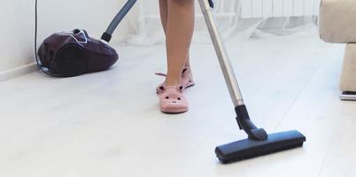 ein Mädchen in Hausschuhen und Bademantel saugt den Boden in einer Wohnung. selektiver Fokus. Filmkorn. foto