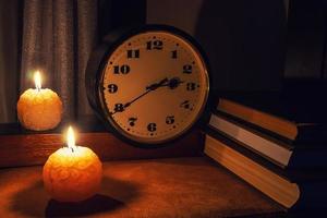 Bücher auf dem Tisch mit einer Uhr, die von Nachtlichtern und Kerzen beleuchtet wird foto