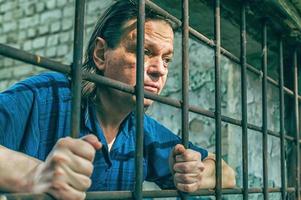 Ein depressiver Mann hält seine Hände an den Gitterstäben des Gefängnisses. Gefangener für das Verbrechen. schlechte Bedingungen. Schrei, Verzweiflung, Schmerz, Hunger. foto