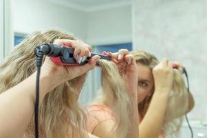 das mädchen am spiegel glättet lockiges haar mit einem haarglätter zu hause. selektiver Fokus, Filmkorn. foto