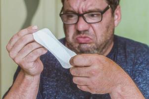 ein Mann mit Brille schaut überrascht auf eine Damenbinde foto