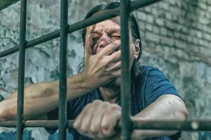 Ein depressiver Mann hält seine Hände an den Gitterstäben des Gefängnisses. Gefangener für das Verbrechen. schlechte Bedingungen. Schrei, Verzweiflung, Schmerz, Hunger. foto
