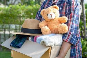 Kleiderspendenbox mit gebrauchter Kleidung und Puppe zu Hause halten, um die Hilfe für arme Menschen in der Welt zu unterstützen. foto