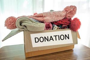 Kleiderspendenbox mit gebrauchter Kleidung und Puppe zu Hause halten, um die Hilfe für arme Menschen in der Welt zu unterstützen. foto