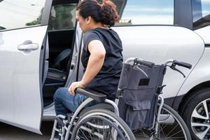 asiatische Frau, die den Rollstuhl in ihr Auto faltet und anhebt. Konzept der Barrierefreiheit. foto