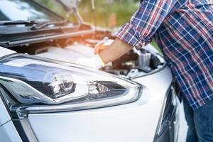 Asiatischer Automechaniker prüft auf Reparatur unter der Motorhaube eines kaputten Autos am Straßenrand. foto