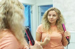 das mädchen am spiegel glättet lockiges haar mit einem haarglätter zu hause. selektiver Fokus, Filmkorn. foto